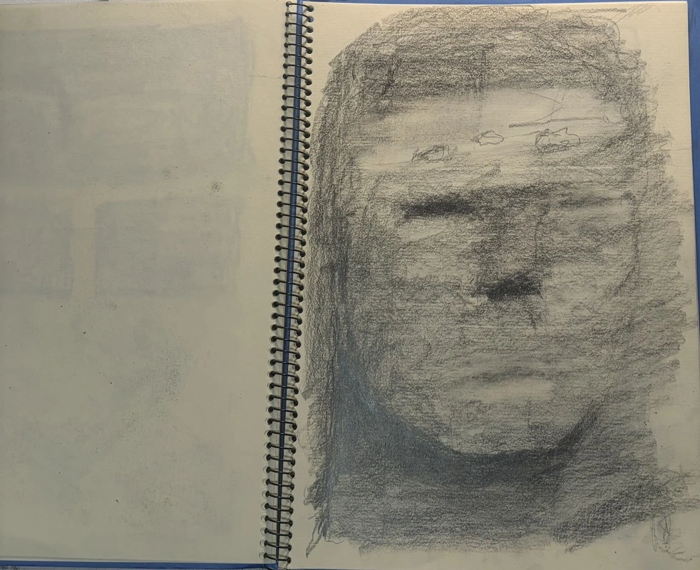 スケッチブックに、風景が重なる大きな顔を描いたドローイング