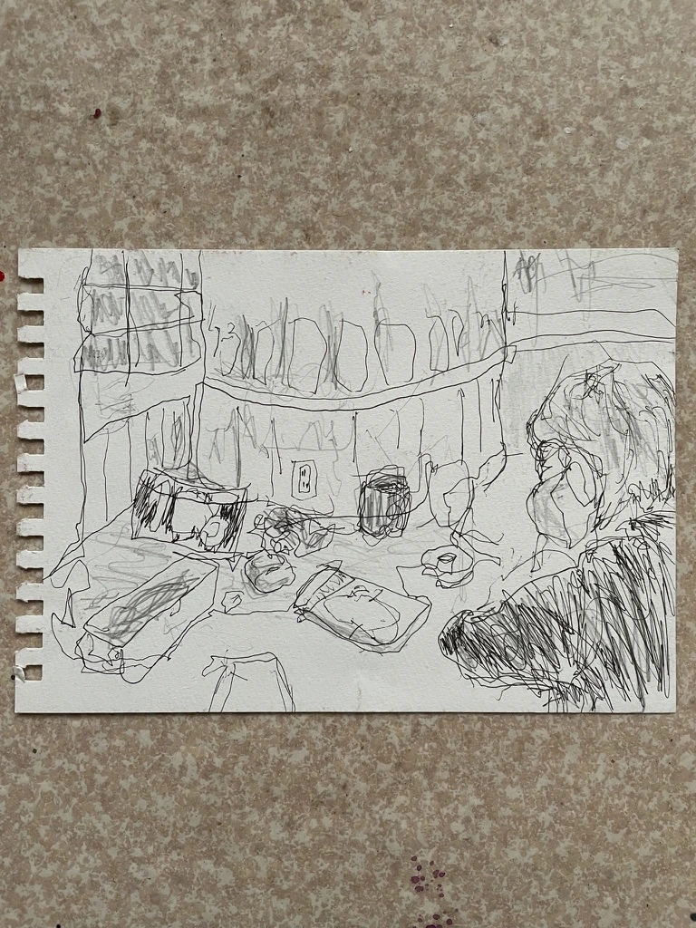 切り離した紙に、机の前の人物と室内を細い線で描いたスケッチ