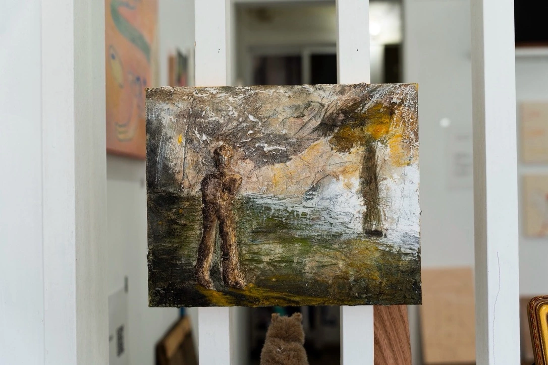 室内に展示した、緑と茶色の風景と人の姿の作品